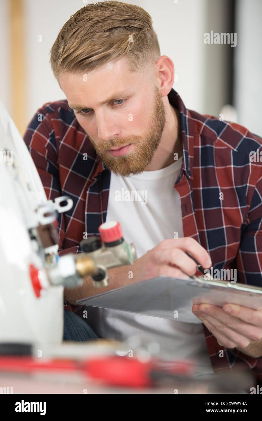 view of plumber writing in clipboard while checking electric boiler Stock Photo