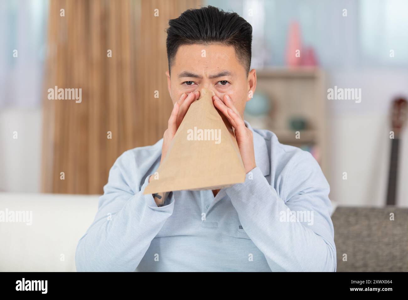stressed man breathing with paper bag while having panic attack Stock Photo
