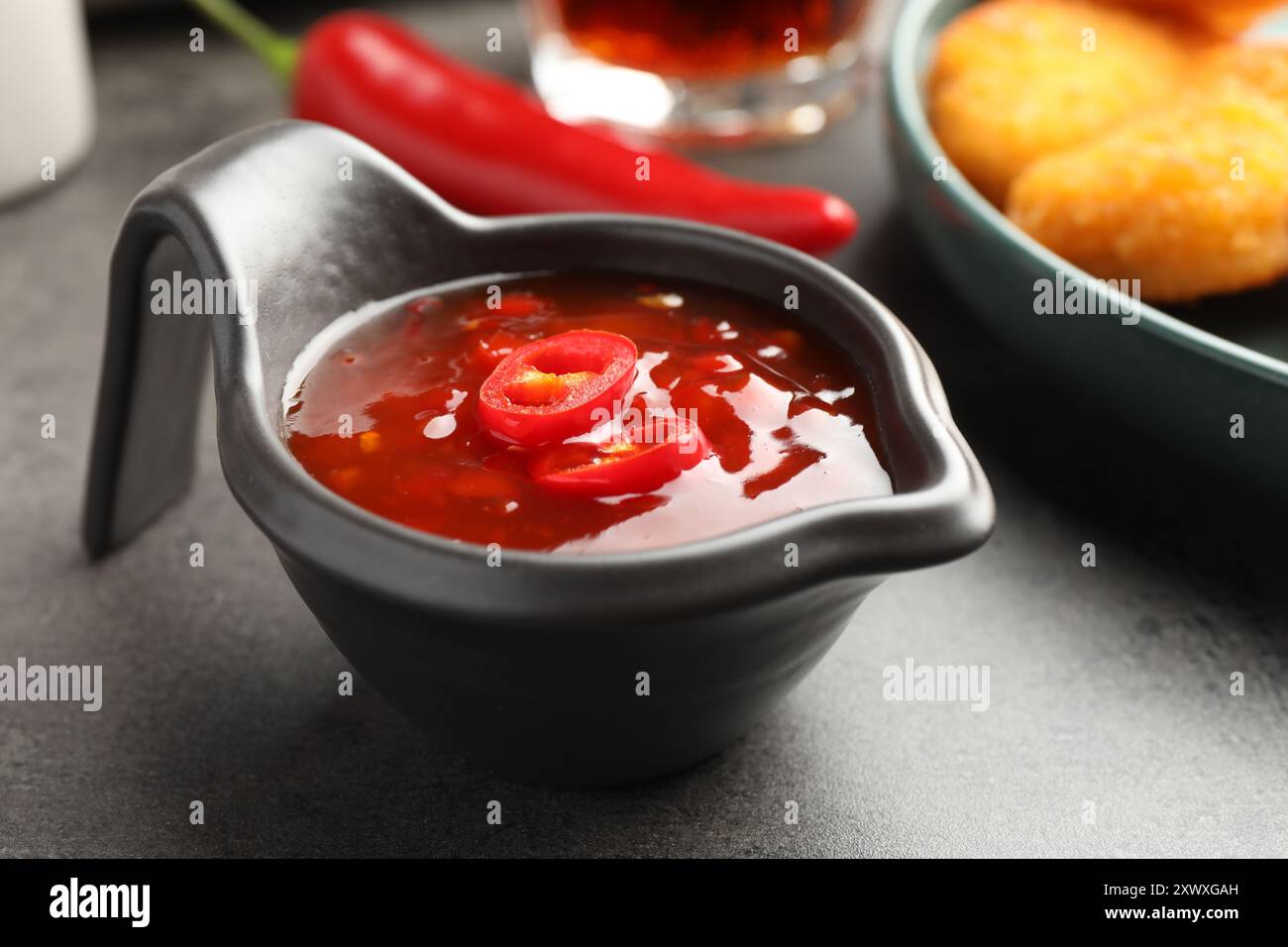 Hot chili sauce in gravy boat on grey textured table, closeup Stock Photo