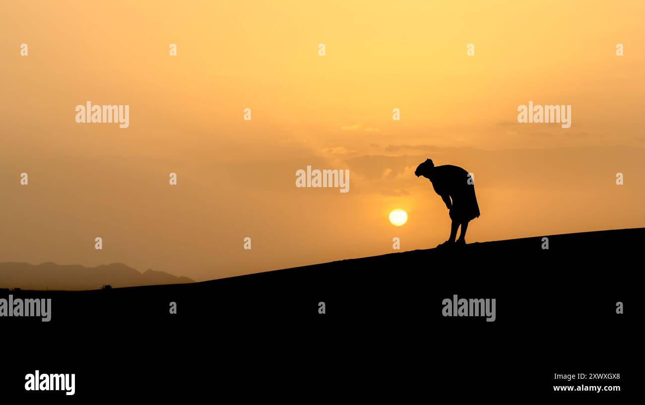 Silhouette of unidentified muslim Berber man praying on sand dunes at ...