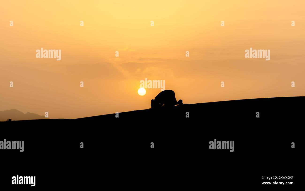 Silhouette of unidentified muslim Berber man praying on sand dunes at ...