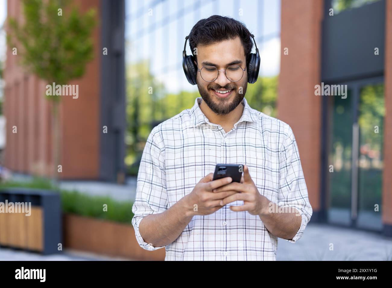 A smiling young Indian man in headphones is walking on a city street ...