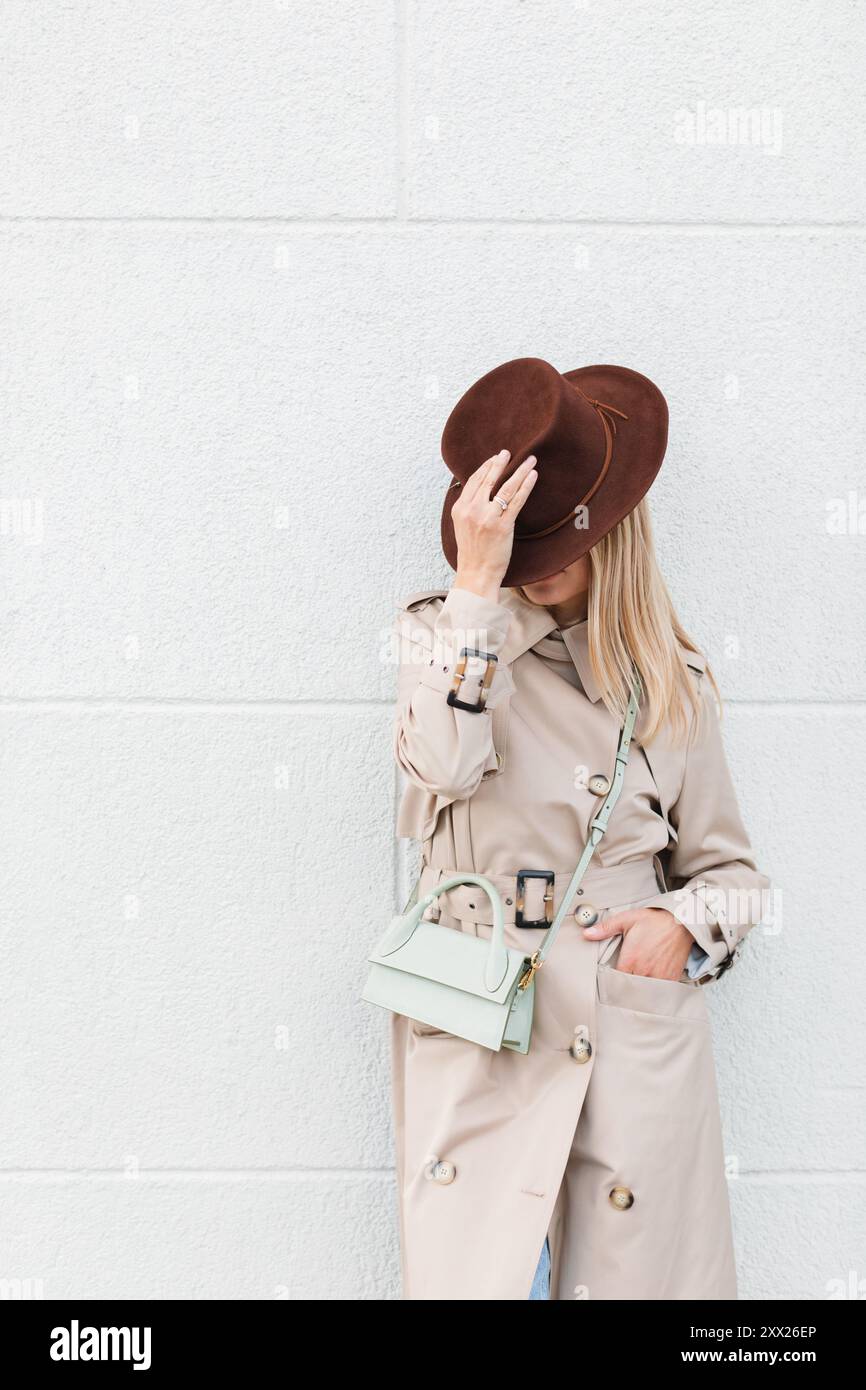 Stylish woman wearing a trench coat leaning against a wall covering her ...