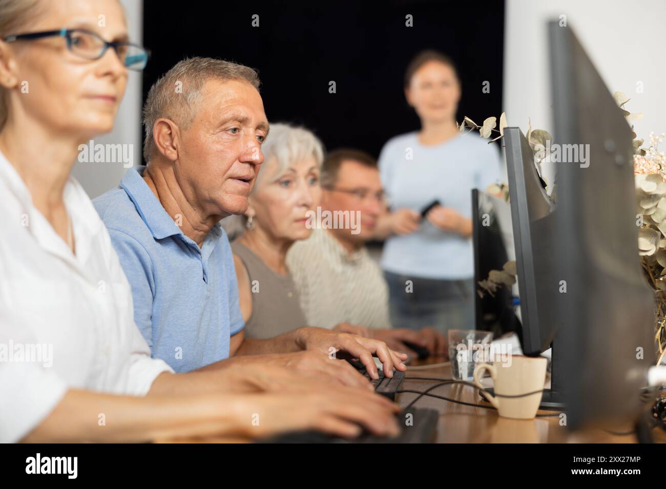 Old man learning computer programs and teacher speaking on the background Stock Photo