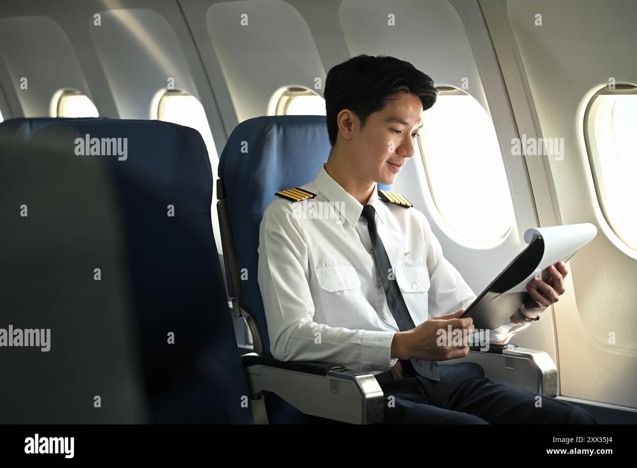 Concentrated pilot dressed in a uniform reading document on an airplane ...