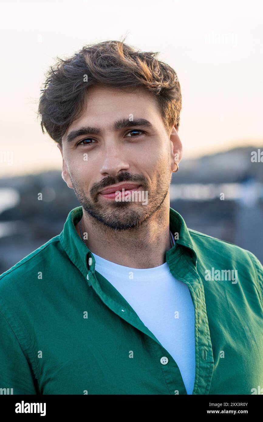 Close-up portrait of a handsome young man with beard and stylish haircut, wearing a green shirt outdoors. Image captures modern male fashion, confiden Stock Photo