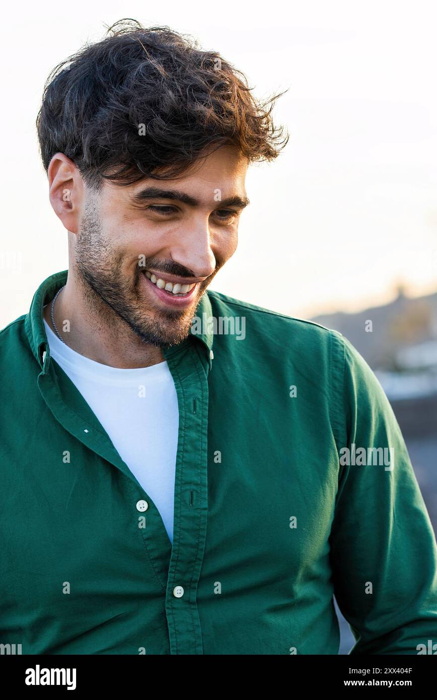 Close-up portrait of a handsome young man with a genuine smile, wearing a green shirt outdoors. Image captures modern male fashion, positive attitude, Stock Photo