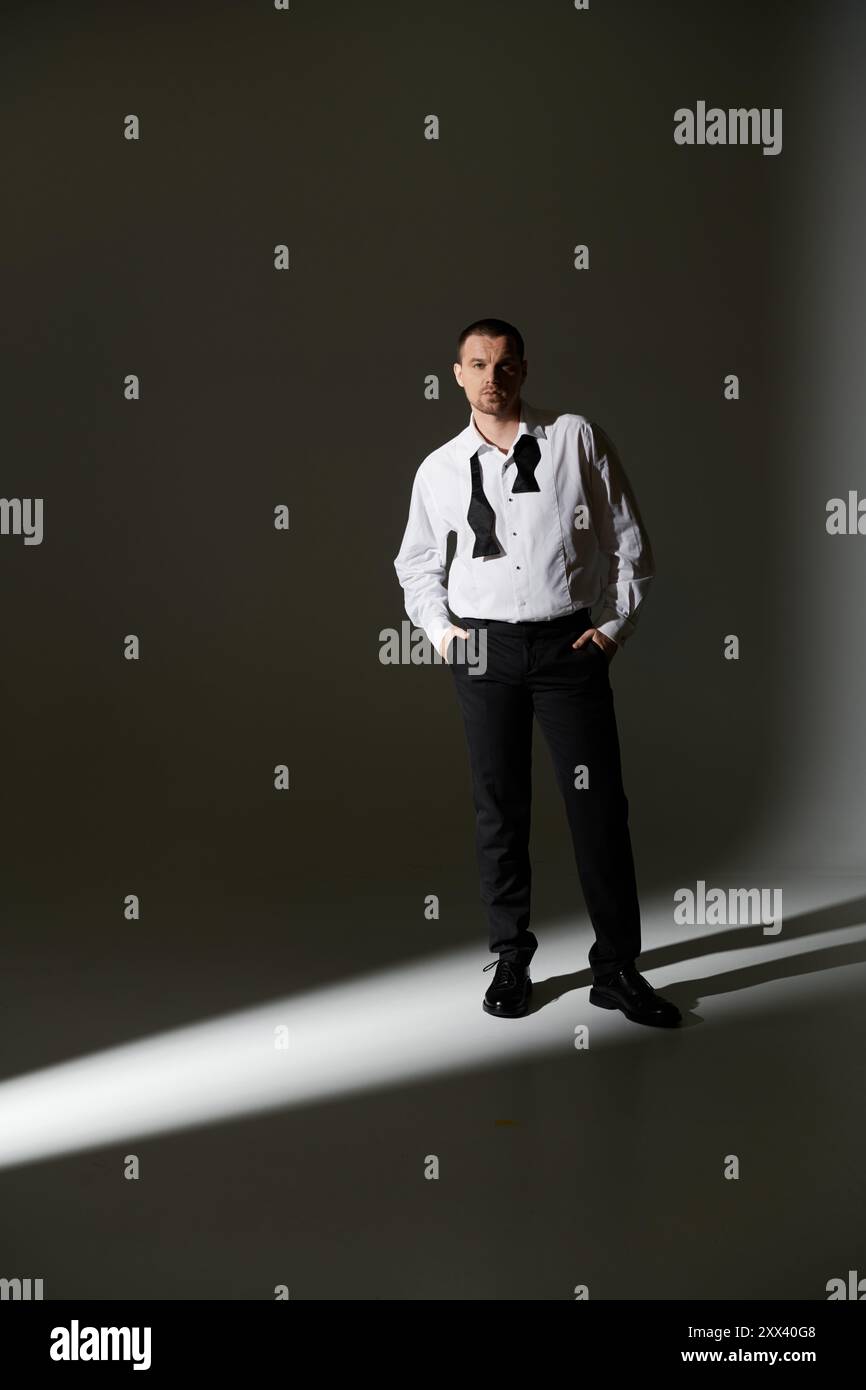 A man in a white shirt and black bowtie stands in a spotlight, looking intensely at the camera. Stock Photo