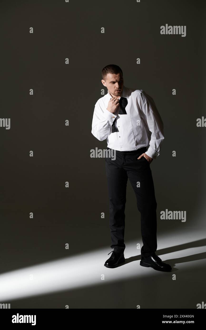 A man in a white shirt and black bow tie stands in a beam of light ...