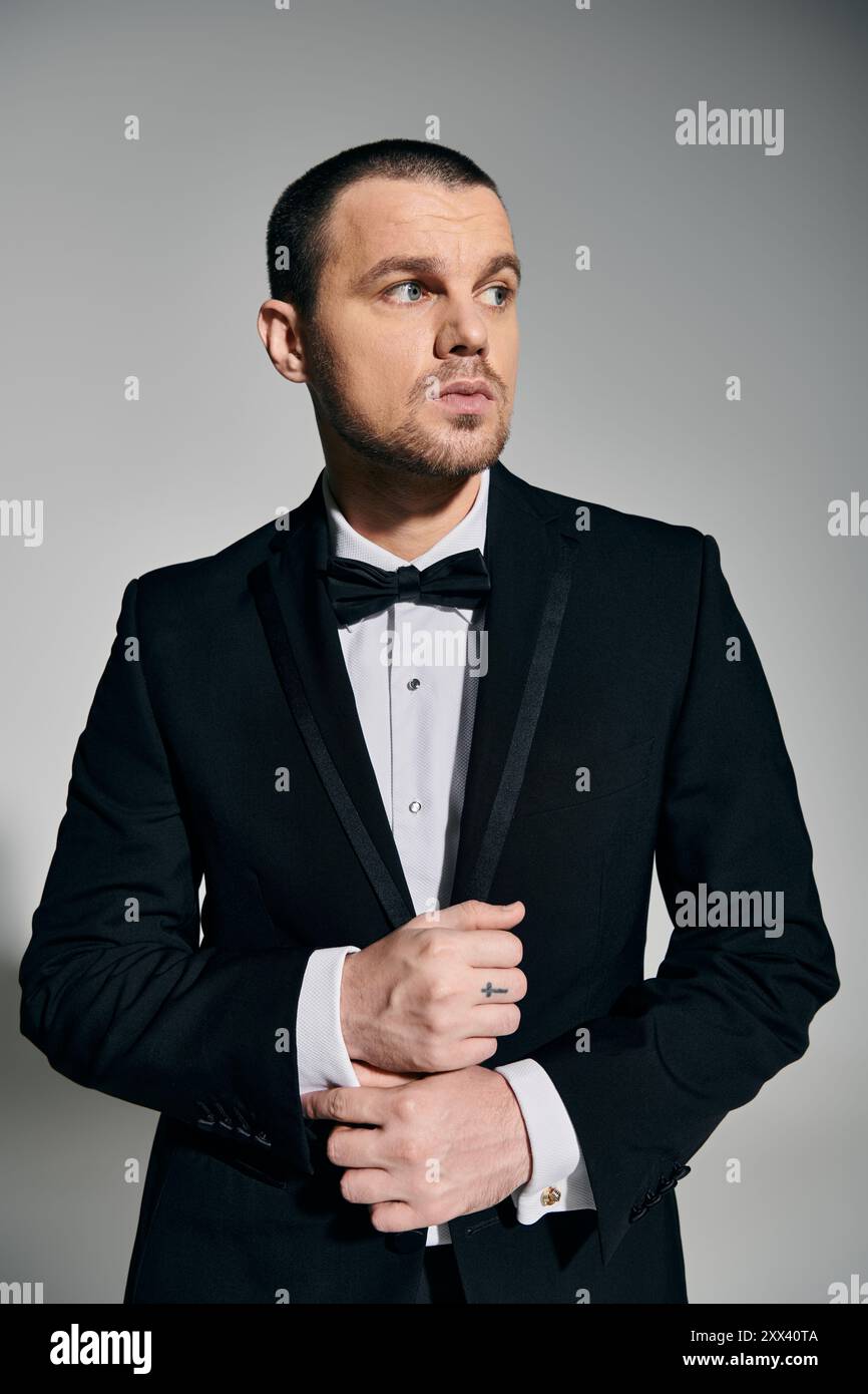 A man in a black suit and bow tie stands with a thoughtful expression ...
