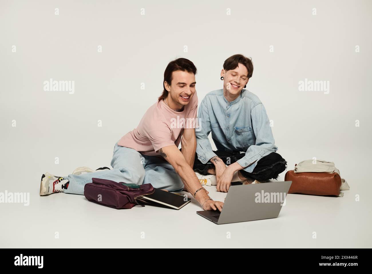 Two young queer students collaborate on a laptop in a studio setting. Stock Photo