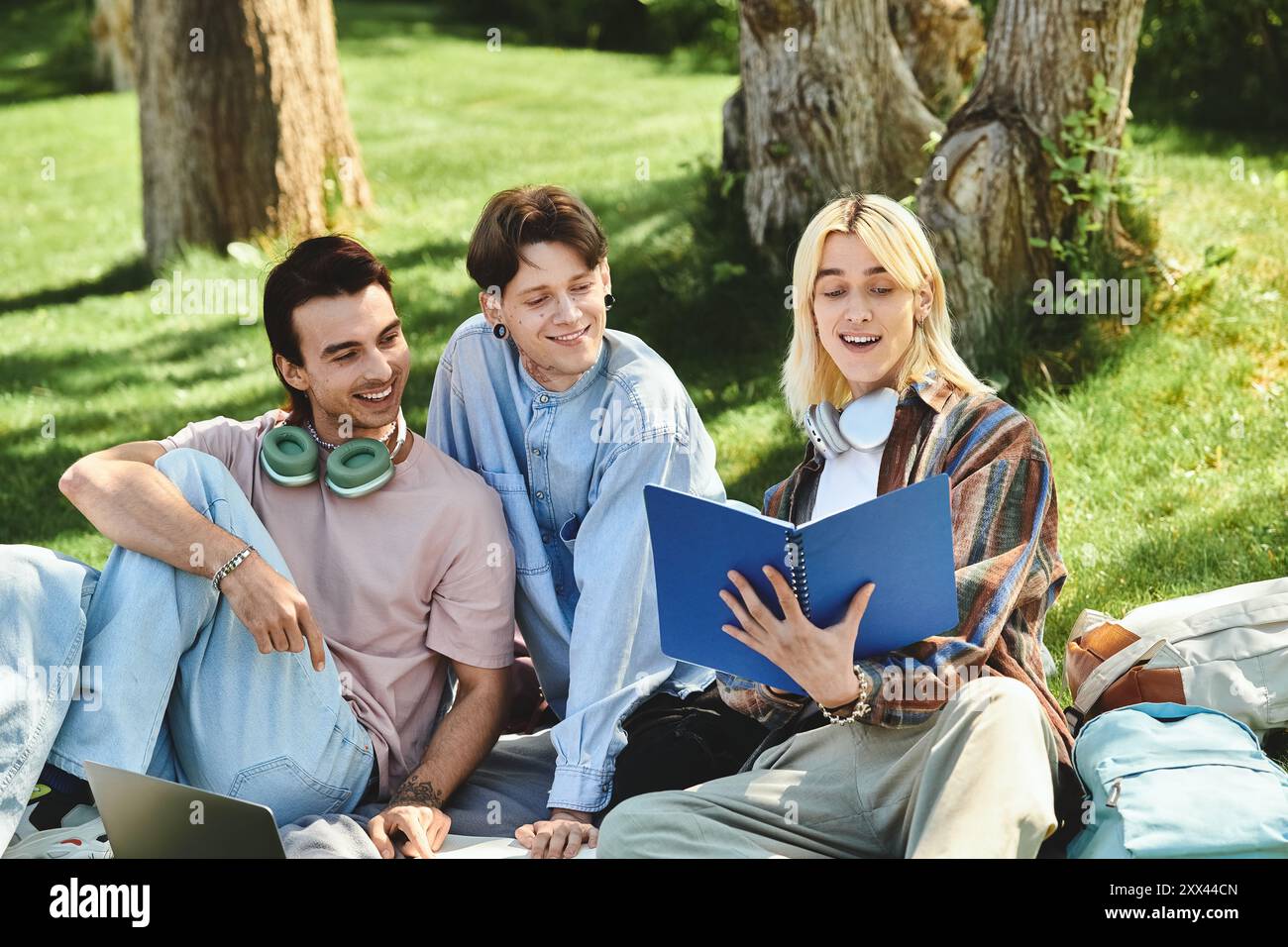 Three young friends, dressed casually, share a laugh while reading a book outdoors. Stock Photo