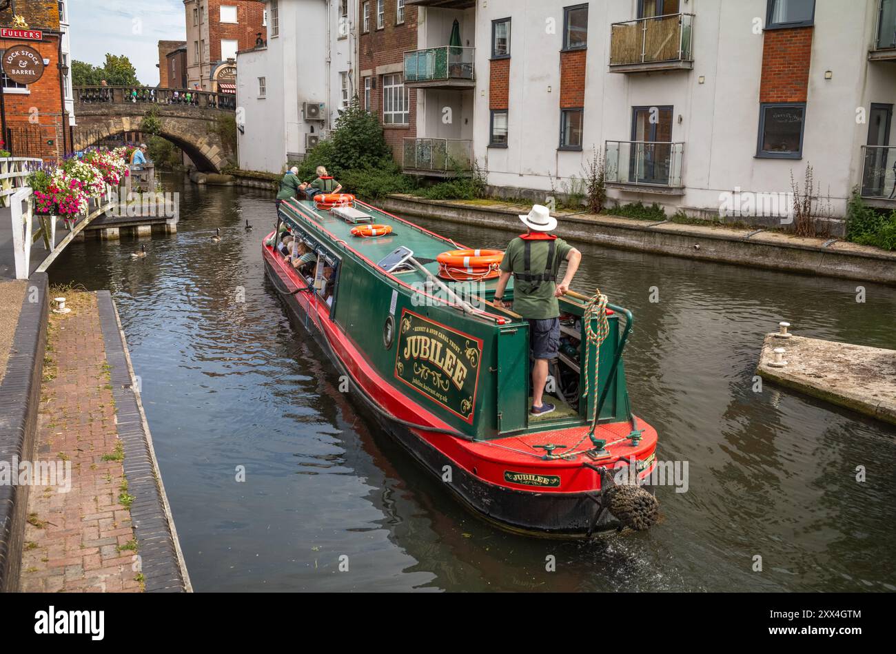 A man steers a holiday canal boat on the Kennet and Avon Canal towards Bridge St, Newbury, Berkshire, England, UK Stock Photo
