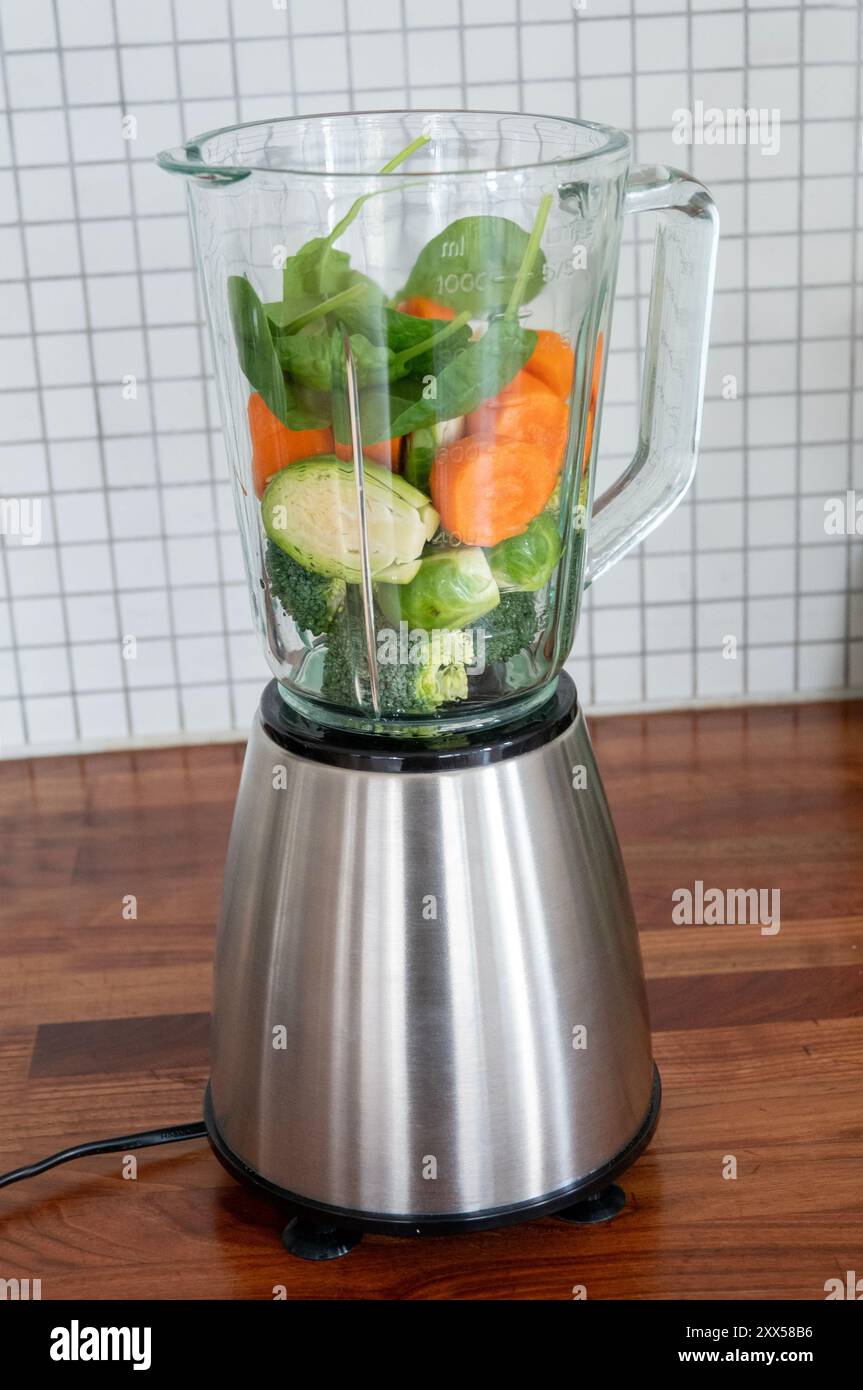 Vitamins packed superfoods in a blender ready to be mixed. Healthy green food spinach, carrots, Brussels sprouts and broccoli. Stock Photo