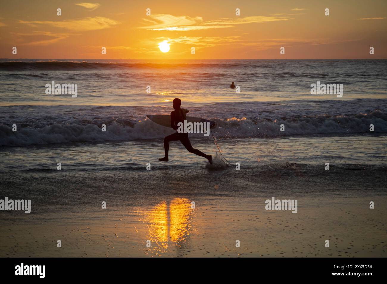 A surfer makes a run for it on the beach of Cox's Bazar in Bangladesh. One of the longest beaches in the world lies at the mouth of the Ganges delta and the waters are rather shallow, which makes for long and predictable waves excellent for beginners and pro's alike. Stock Photo