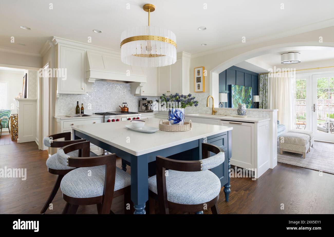 Angled view of white kitchen with blue island and view into TV room ...