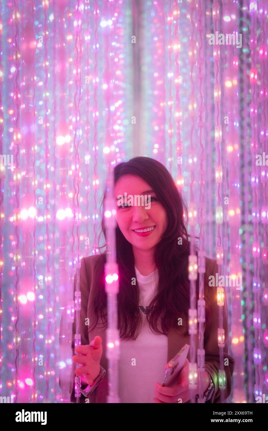 A woman poses surrounded by colorful LED lights in an immersive digital art installation that creates a magical, futuristic atmosphere, Tokyo Japan Stock Photo