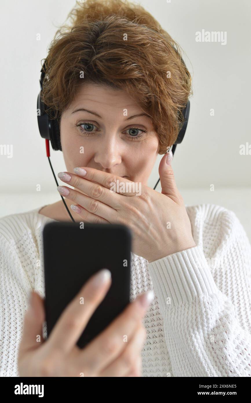 Woman in a headphones with surprise looks at smartphone Stock Photo