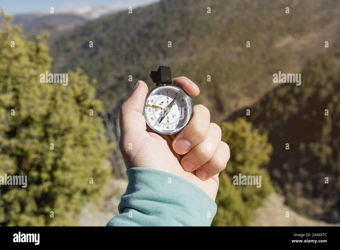 Close-up A man's hand holds a pocket compass against the backdrop of mountains and woods. The concept of outdoor navigation Stock Photo