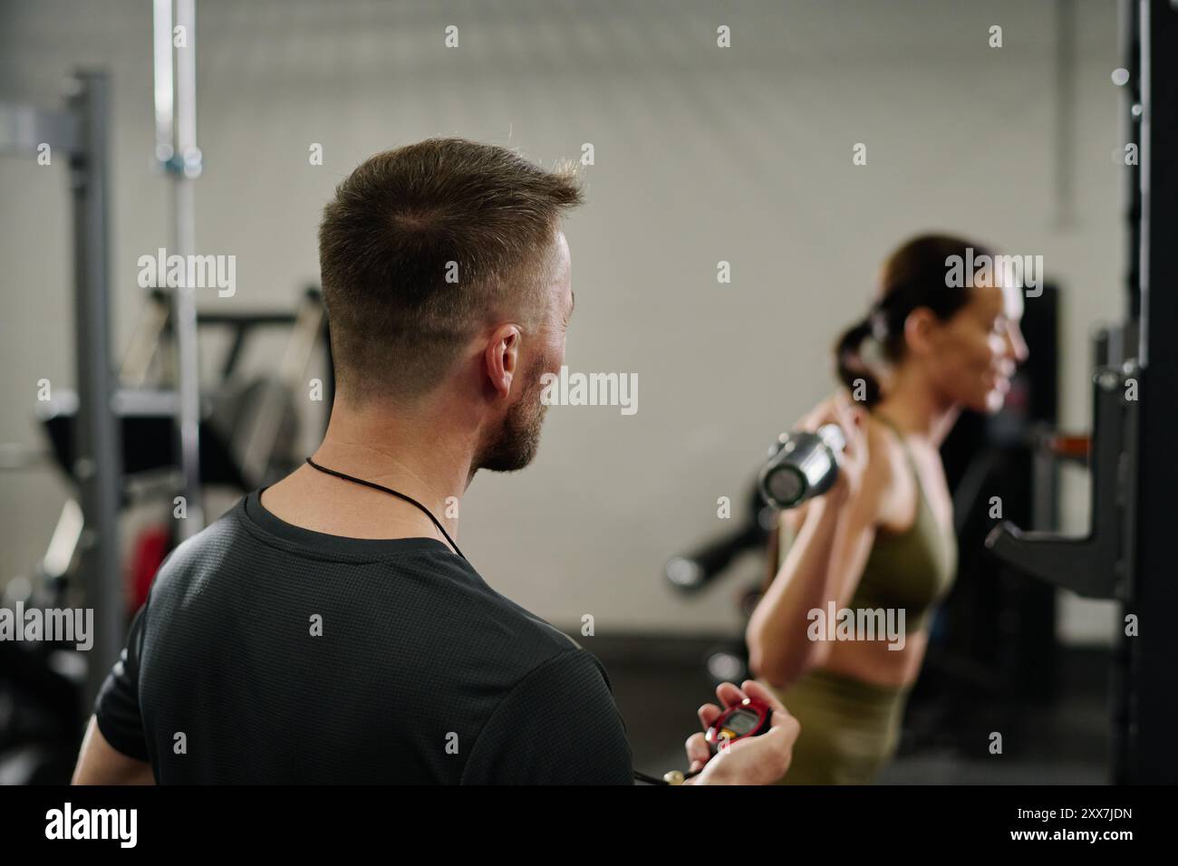 Unrecognizable trainer noting time while athlete doing squats in gym Stock Photo
