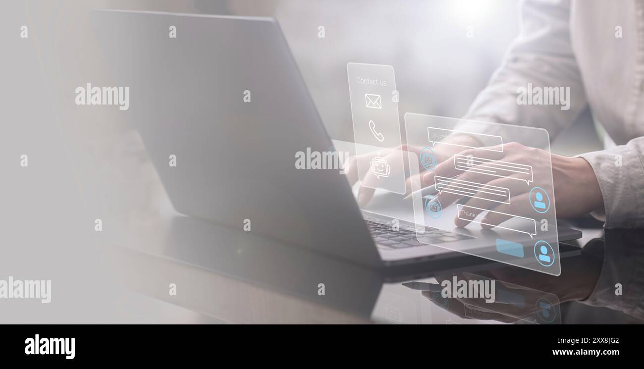 A businessman is working at his laptop, with a hologram of a chatbot illuminating in front of him. He is using AI technology to manage and enhance his Stock Photo