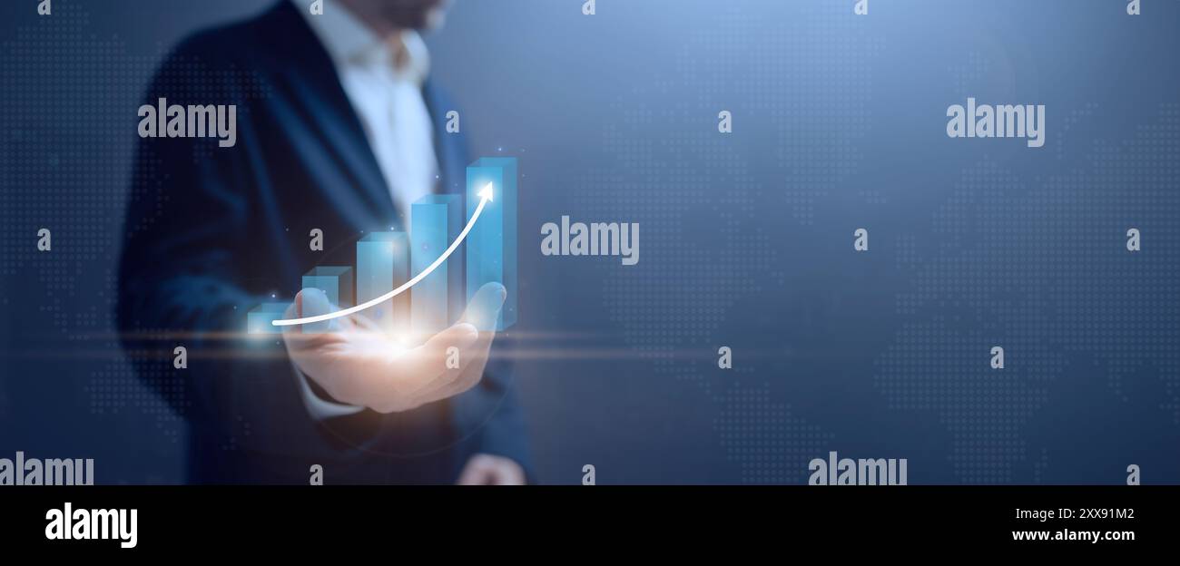 A businessman stands against a dark blue background, with a holographic business growth chart appearing on his hand. The futuristic display symbolizes Stock Photo