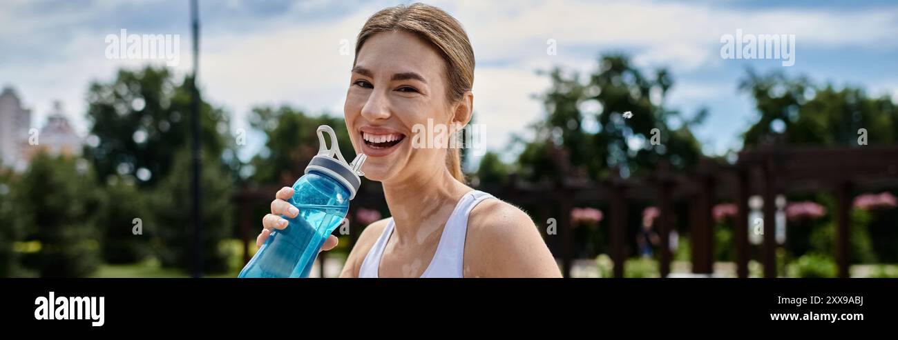 A young woman in activewear smiles and takes a drink of water from a ...
