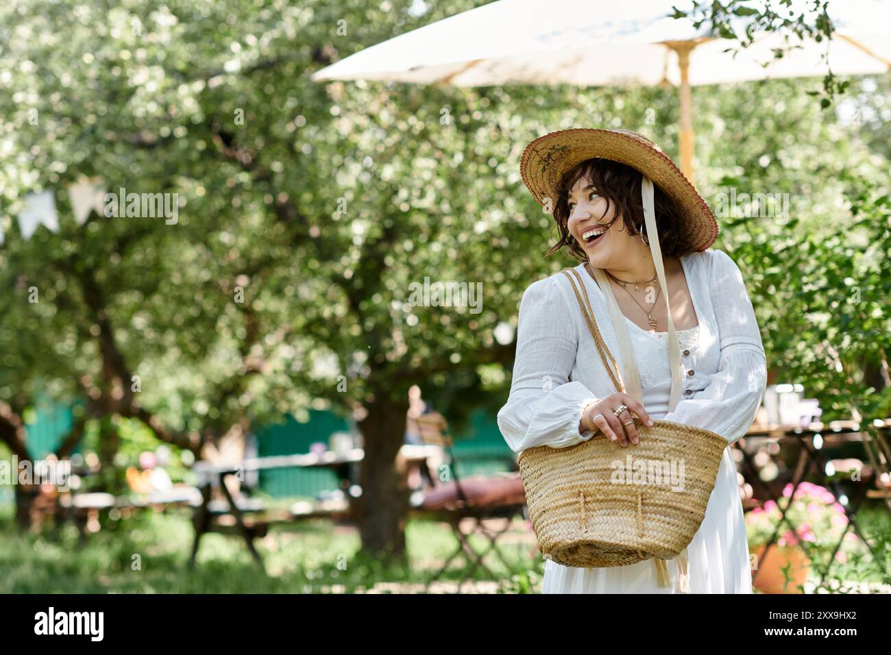A woman in a white blouse and straw hat smiles brightly as she walks ...