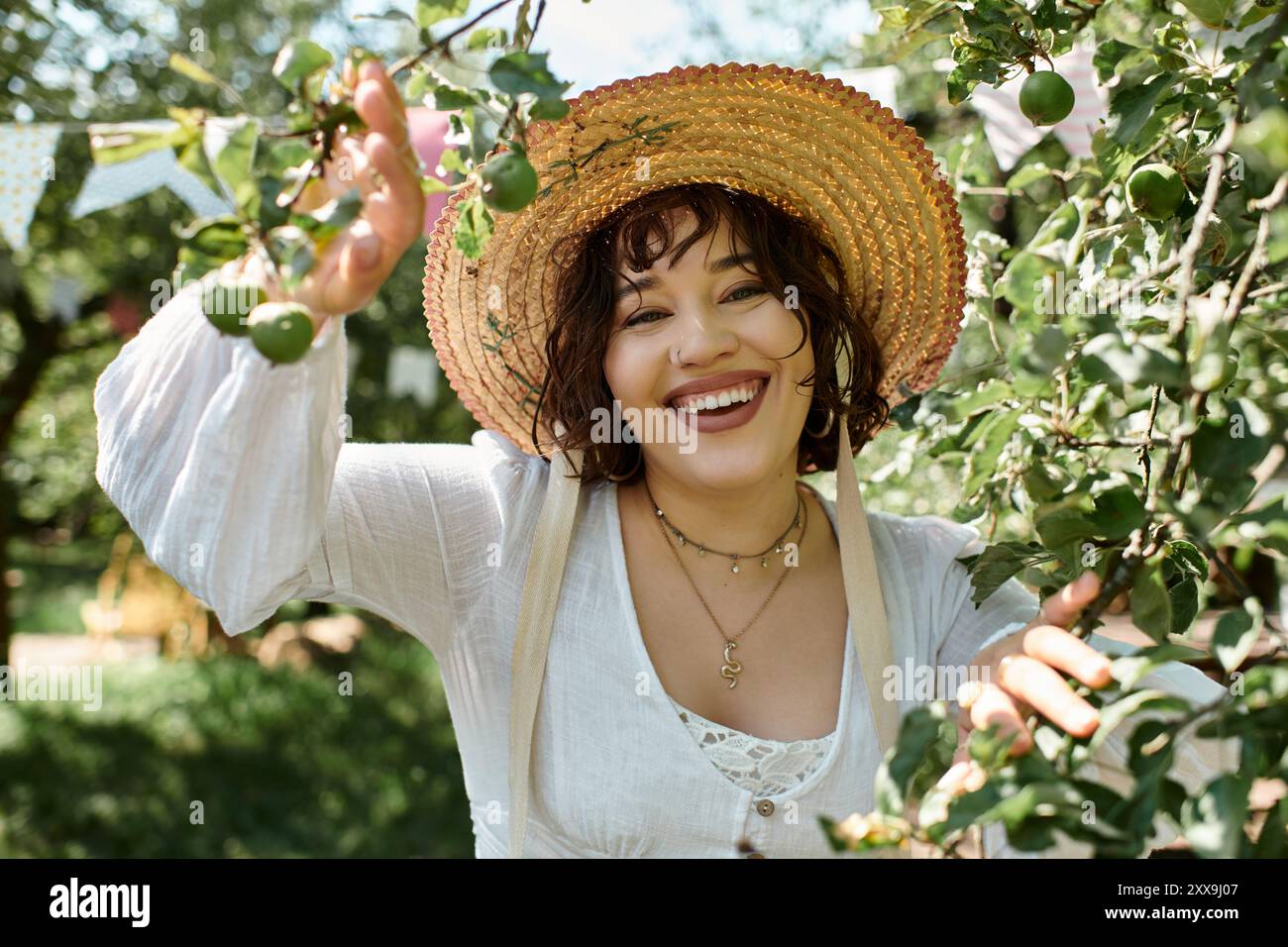 A young woman in a white blouse and straw hat smiles brightly as she ...
