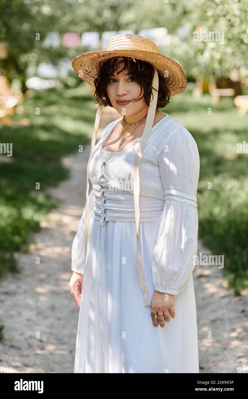 A young woman in a white dress and straw hat walks through a sunny ...