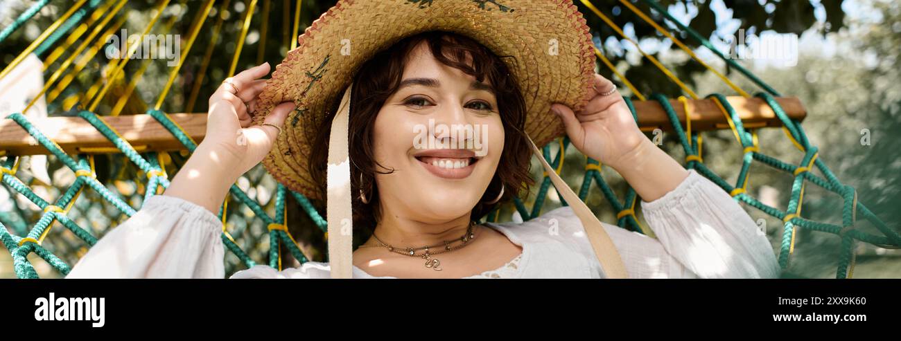 A brunette woman in a white dress and straw hat smiles while relaxing ...
