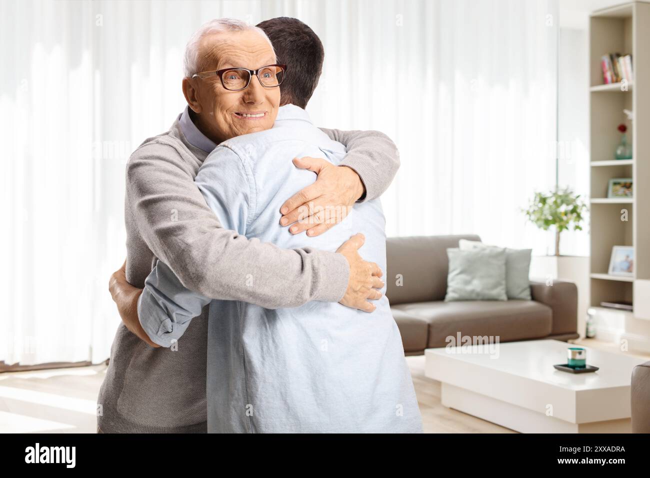 Elderly man hugging a younger man in a living room Stock Photo