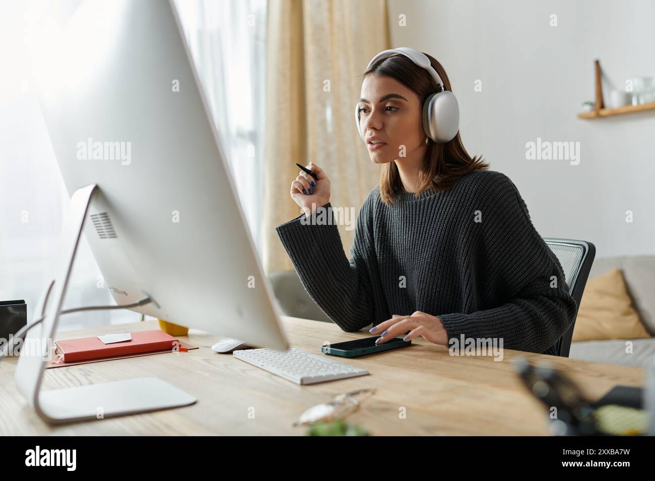 A young woman works from home, focused on her computer screen ...