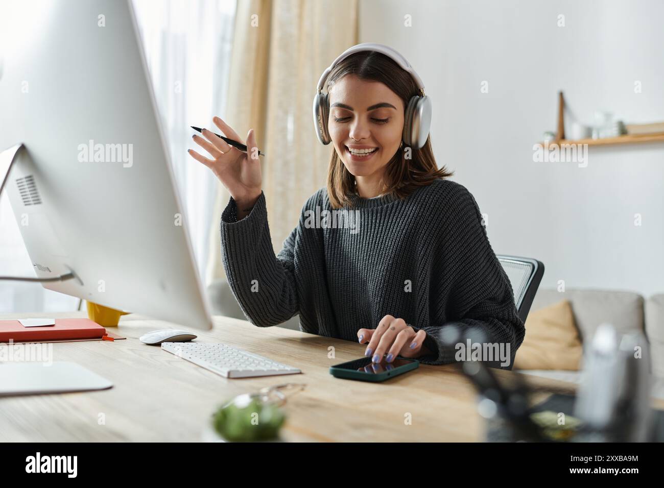 A young woman wearing headphones smiles and gestures while working at ...