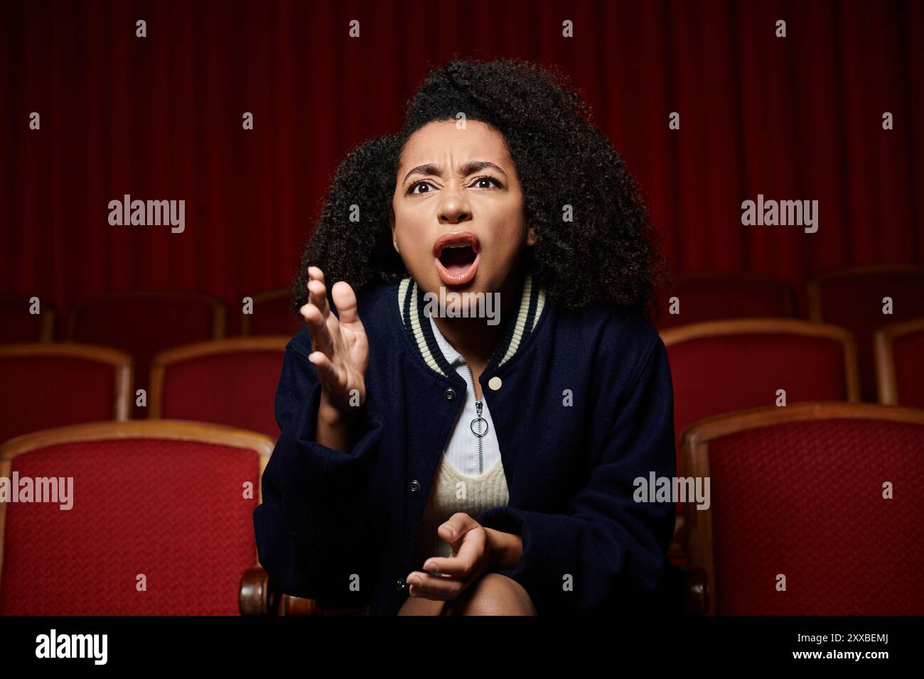 A young woman sits in a cinema seat, mouth agape, reacting to the movie ...