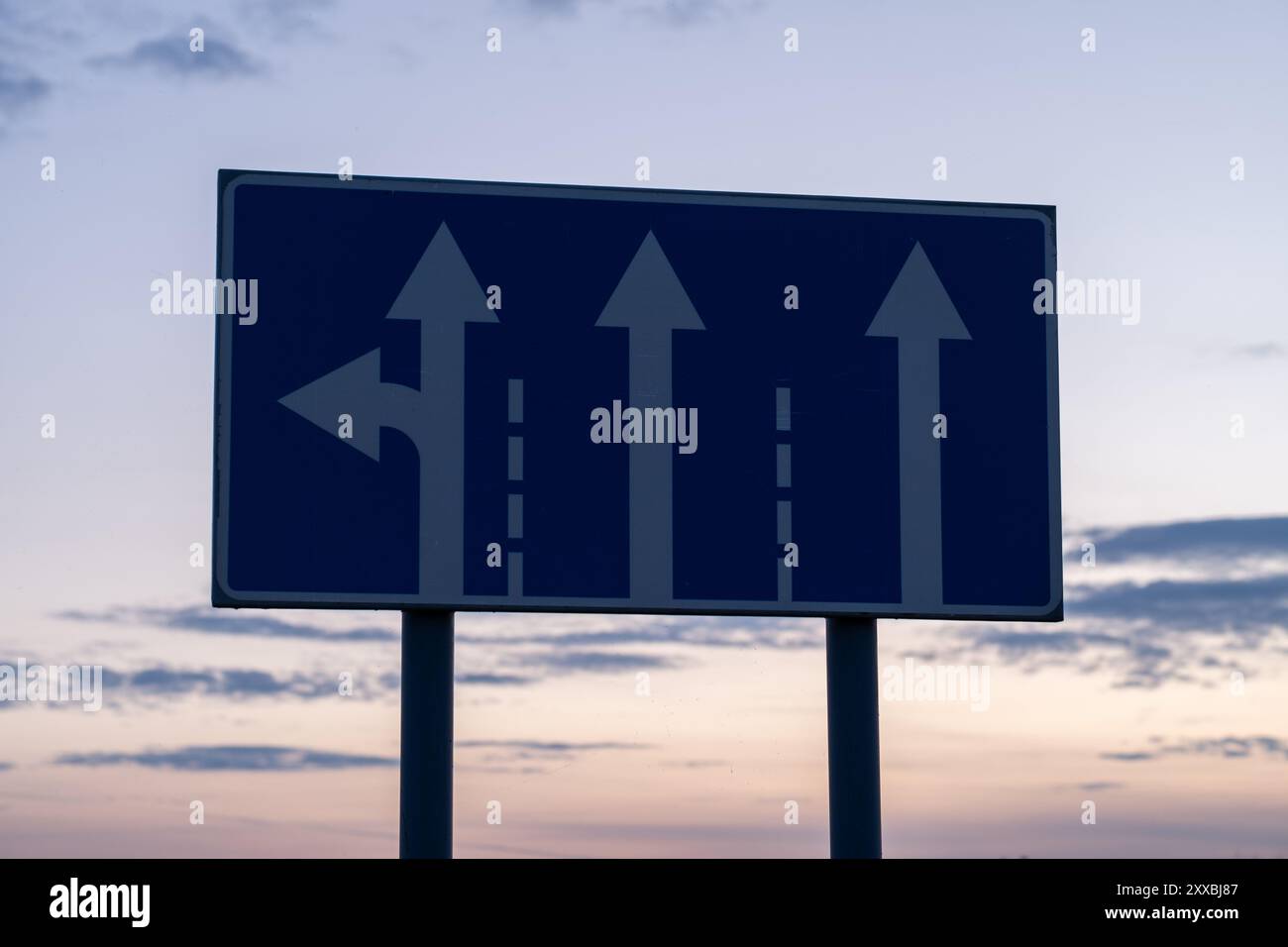 Road sign with arrows pointing to different directions on sunset sky ...