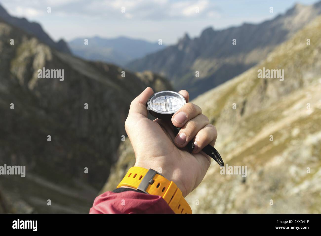 A man's hand holds a pocket magnetic compass for navigation against the backdrop of a rocky slope and a mountain. The concept of finding a way. Gainin Stock Photo