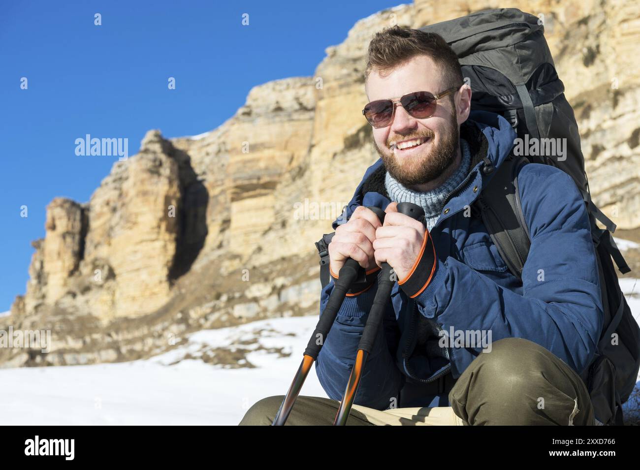 Portrait of happy laughing Hipster traveler with beard in sunglasses is sitting on nature. A man hiking in the mountains with a backpack and Scandinav Stock Photo