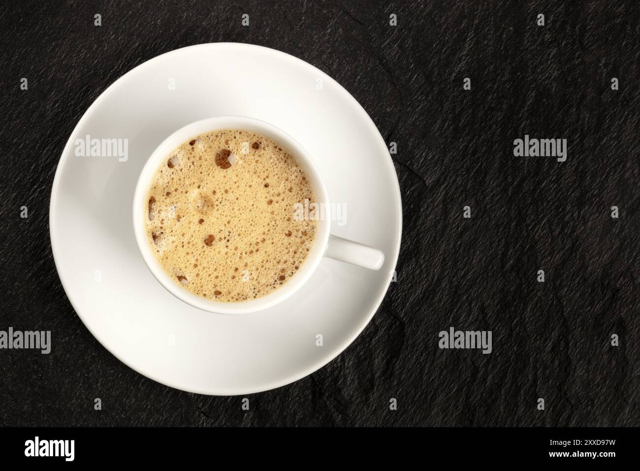 A cup of regular coffee with foam on a dark black background with a place for text Stock Photo