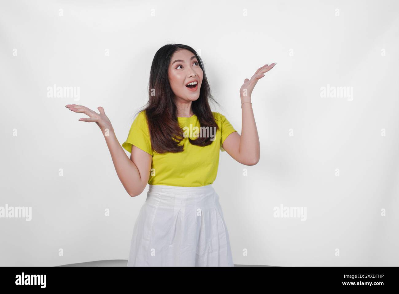 Joyful Asian woman in a yellow shirt and white skirt showing excited ...