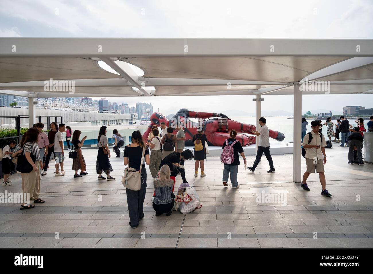 Locals and tourists pose for photos with the 8-meter installation of Marvel's Deadpool character, set up to promote the new movie 'Deadpool & Wolverine' released under Disney in Hong Kong. Stock Photo