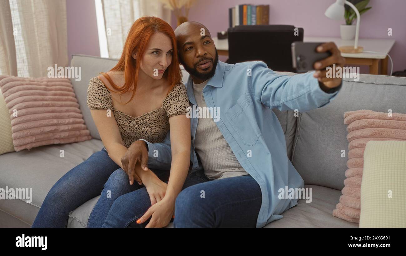 Couple taking a selfie in their living room, showcasing an interracial relationship with a loving atmosphere in their home as they sit together on a c Stock Photo