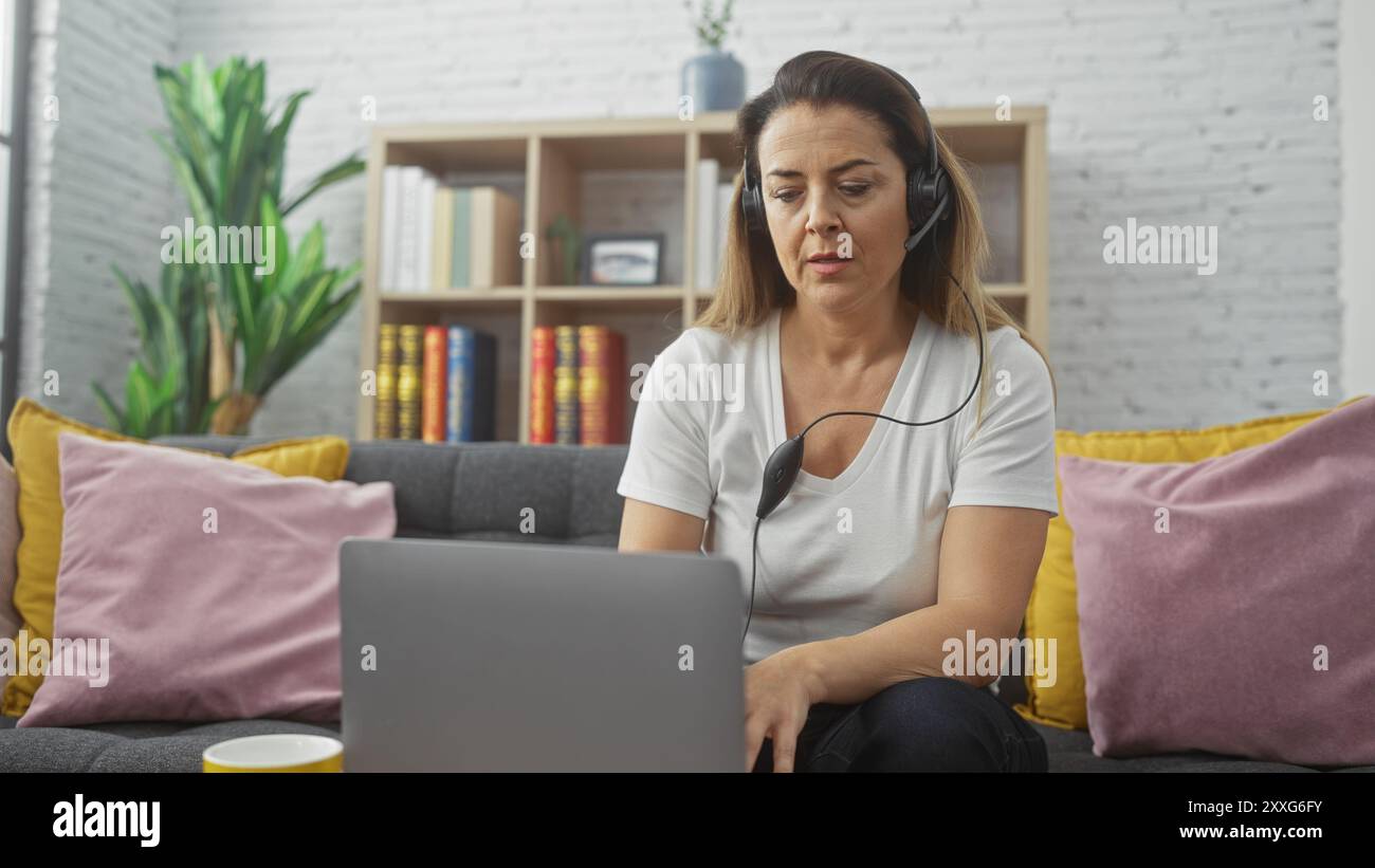 A focused hispanic woman wearing headphones works on her laptop in a ...