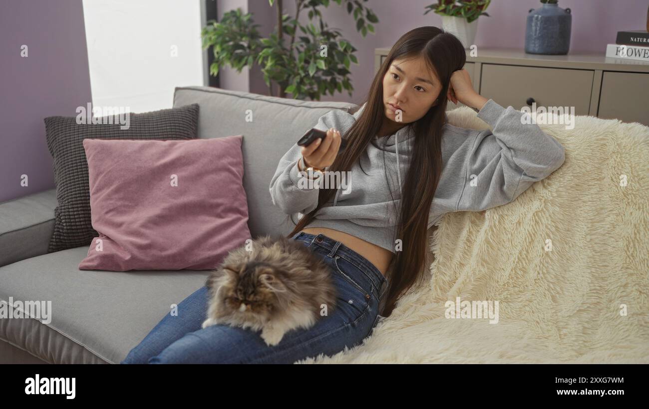 A young chinese woman relaxes in her living room with a fluffy cat on ...
