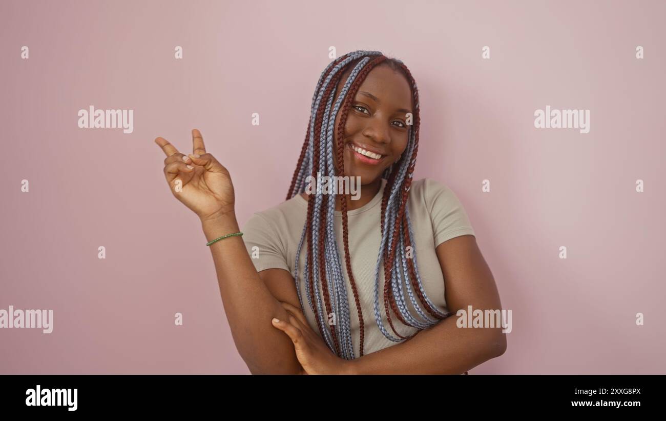 Smiling african woman with braids gesturing peace against a pink ...
