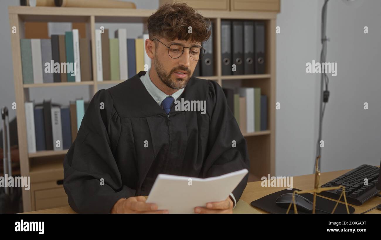 Young man in glasses wearing judge robe reading document at office desk ...