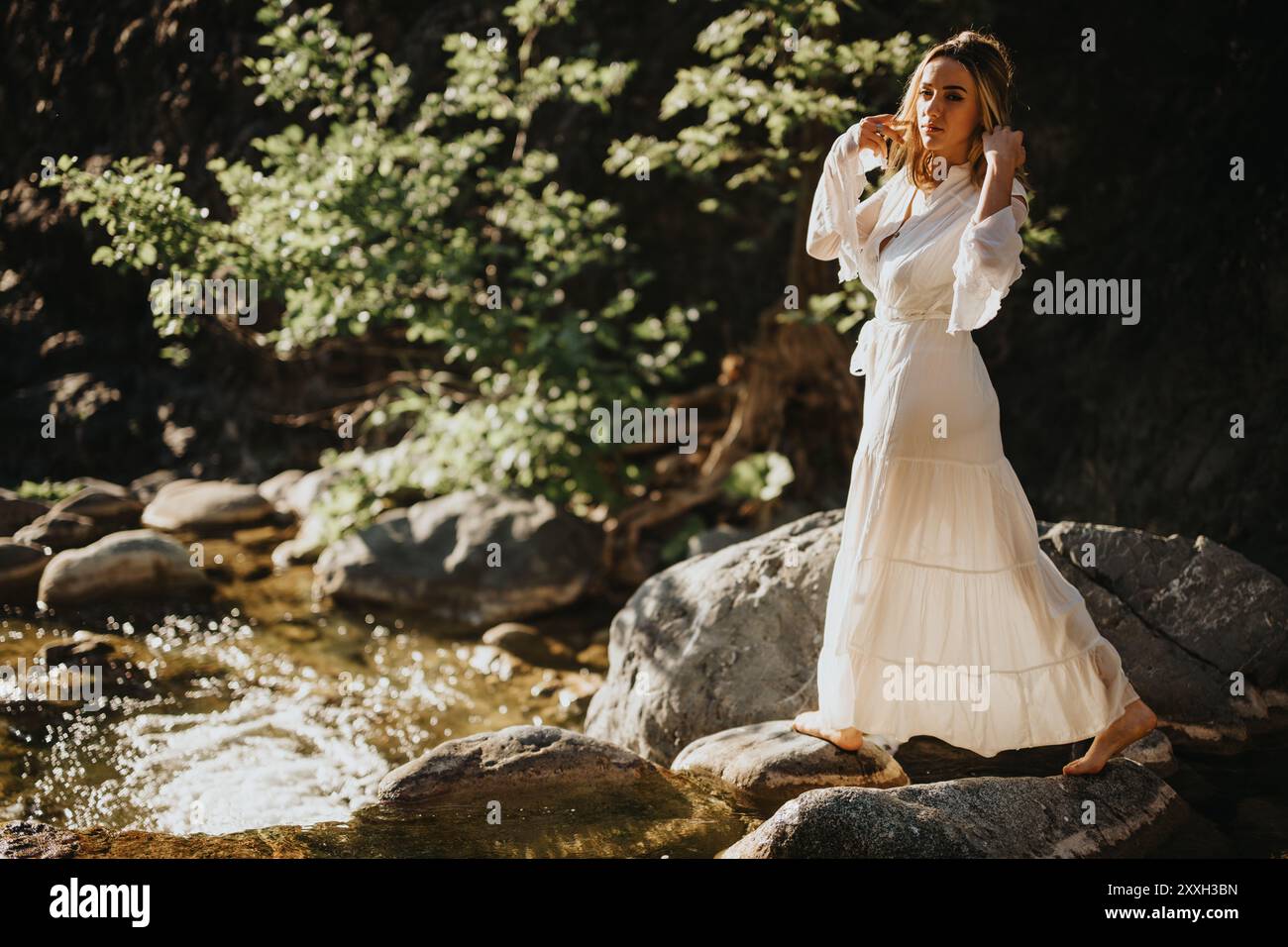 Woman in white dress standing on rocks by a stream in a natural setting ...