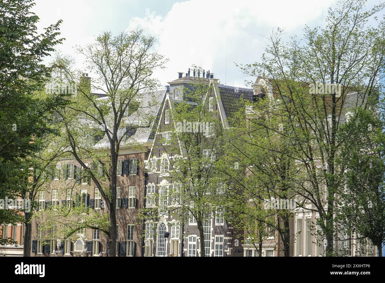 Historic buildings between many green trees under a slightly cloudy sky, Amsterdam, Netherlands Stock Photo