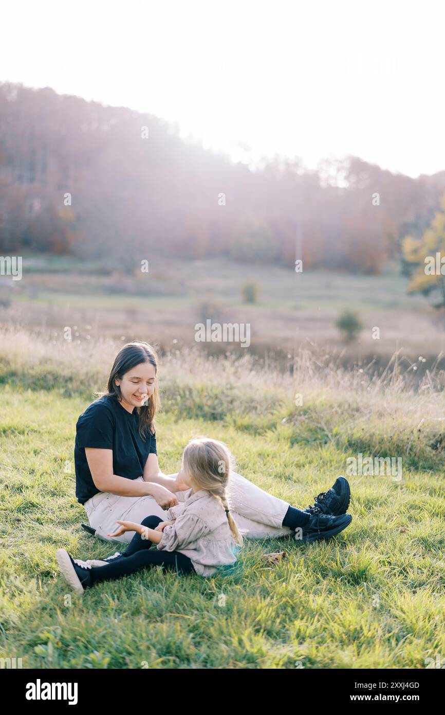 Little girl sits near her mother on a green lawn and tells her ...