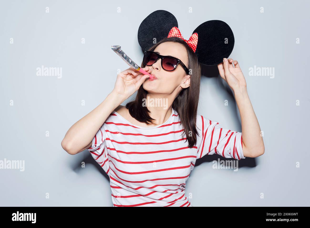 Young woman with party blower against light blue background Stock Photo ...